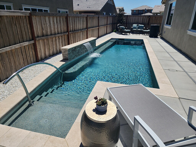 Finished custom shaped pool matching the rendering with bumped out steps, handrail, raised wall with sheer descent water feature and seating bench