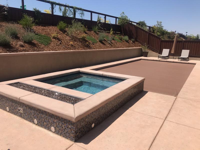 Rectangular pool with raised spa with a fire feature and automatic pool cover.