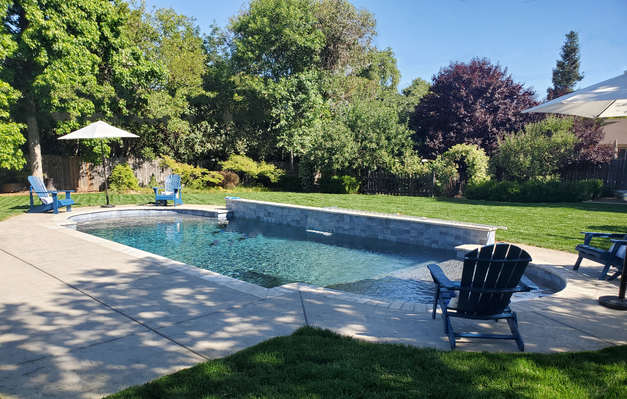 Grecian shaped pool with large Cabo shelf and raised wall with sheer descent water feature.