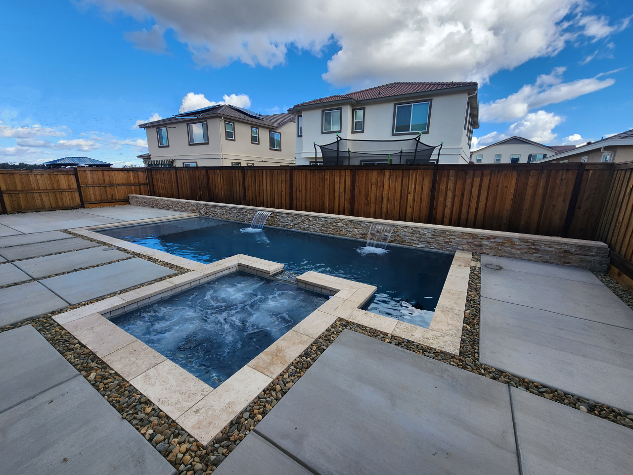 Rectangular shaped pool and spa and raised wall with two sheer descent water features and travertine stone coping.