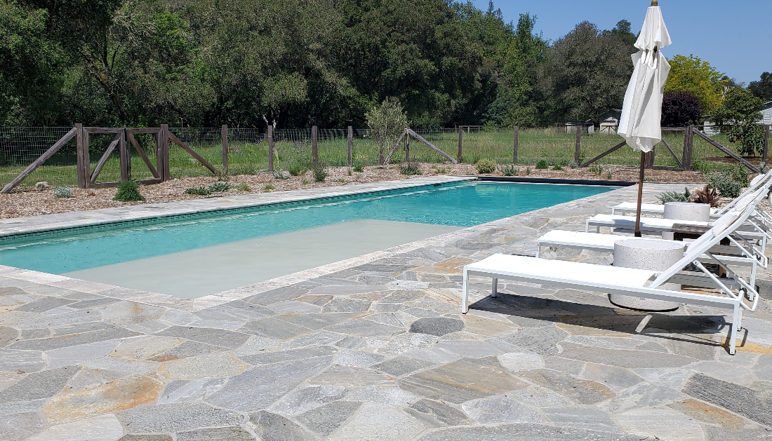 Rectangular shaped pool with turquoise blue water and a large Cabo shelf and automatic pool cover with an aluminum lid and flagstone decking.