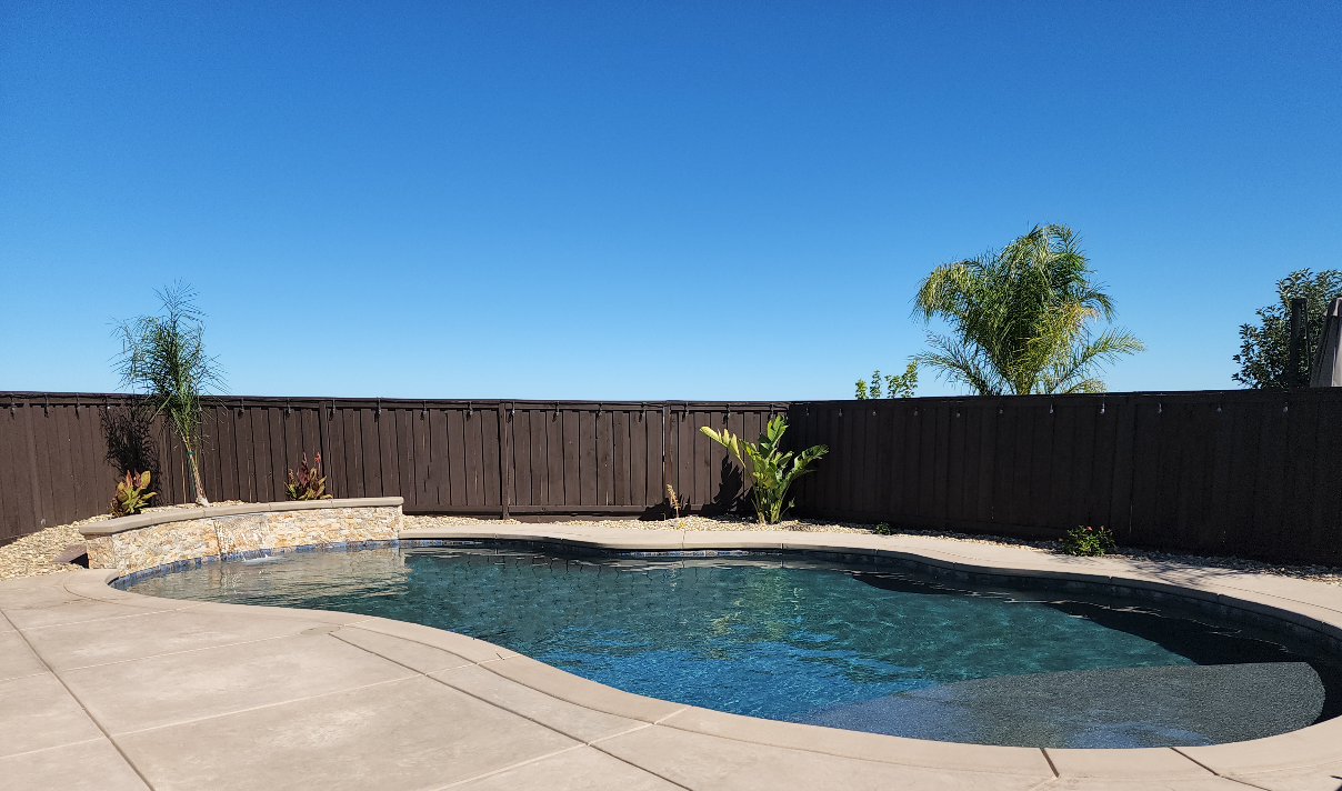 Freeform shaped pool with raised wall with a sheer descent water features and a large Cabo shelf.