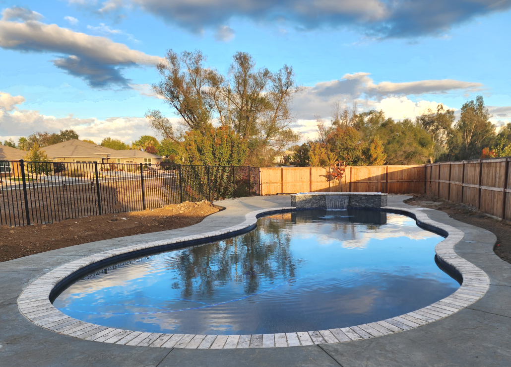Freeform shaped pool with raised wall with sheer descent water feature and stone coping.
