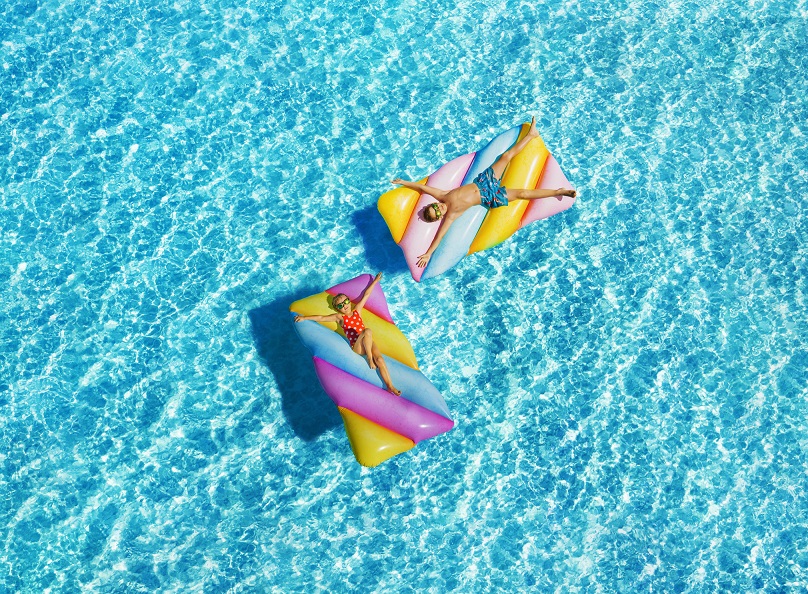 Two children on colorful striped inflatable floats relaxing in a sunlit swimming pool
